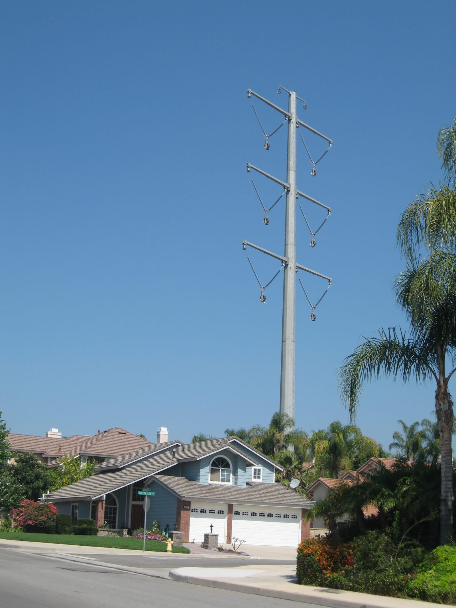 A nearly 200-foot steel 500 kV pole beside a two-story house at a Chino Hills street corner against a clear sky.